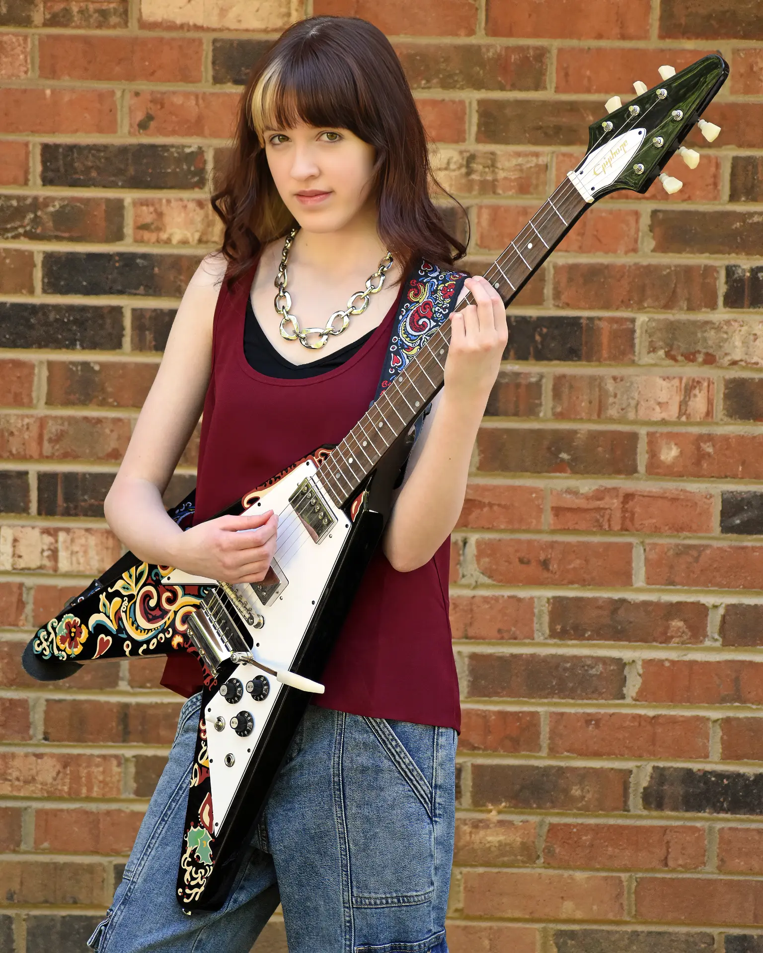 Josette Seraphine with her Flying V electric guitar against a brick wall